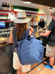 Person folding large navy tote behind their back and over their shoulder while waiting at a counter with wine