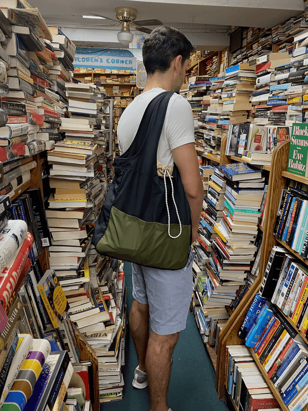 Packable, foldable, reusable tote made from recycled ocean plastic, carried in a cozy bookstore aisle.
