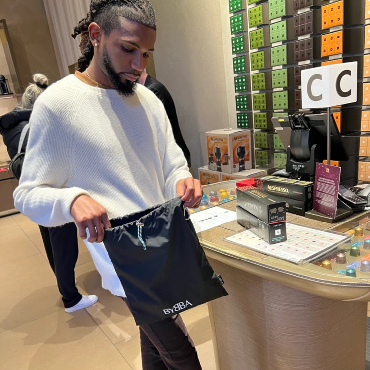 Man holding black BYBBA packable, foldable, reusable bag made from recycled ocean plastic at store counter