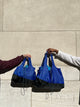 hands from two different people holding two sizes of deep blue bags