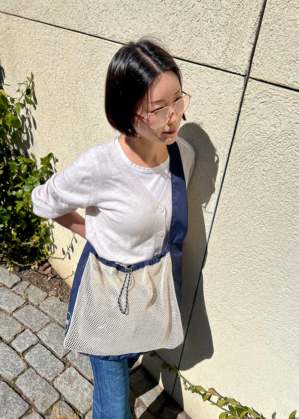 woman standing against a wall wearing net bag across their body and hanging at their waist