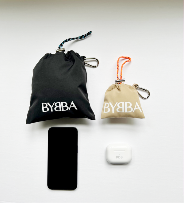 small black pouch displayed next to cell phone and smaller pale pouch displayed next to ear buds