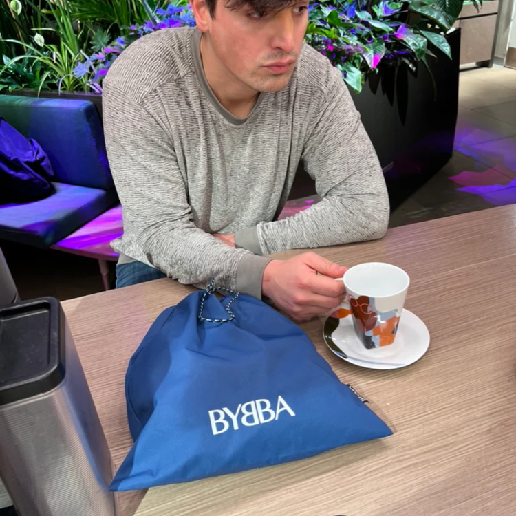 Blue BYBBA packable, foldable, reusable bag made from recycled ocean plastic on table with coffee