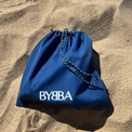 Blue BYBBA drawstring bag on sand, packable, foldable, reusable, made from recycled ocean plastic