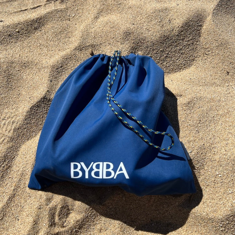 Blue BYBBA drawstring bag on sand, packable, foldable, reusable, made from recycled ocean plastic