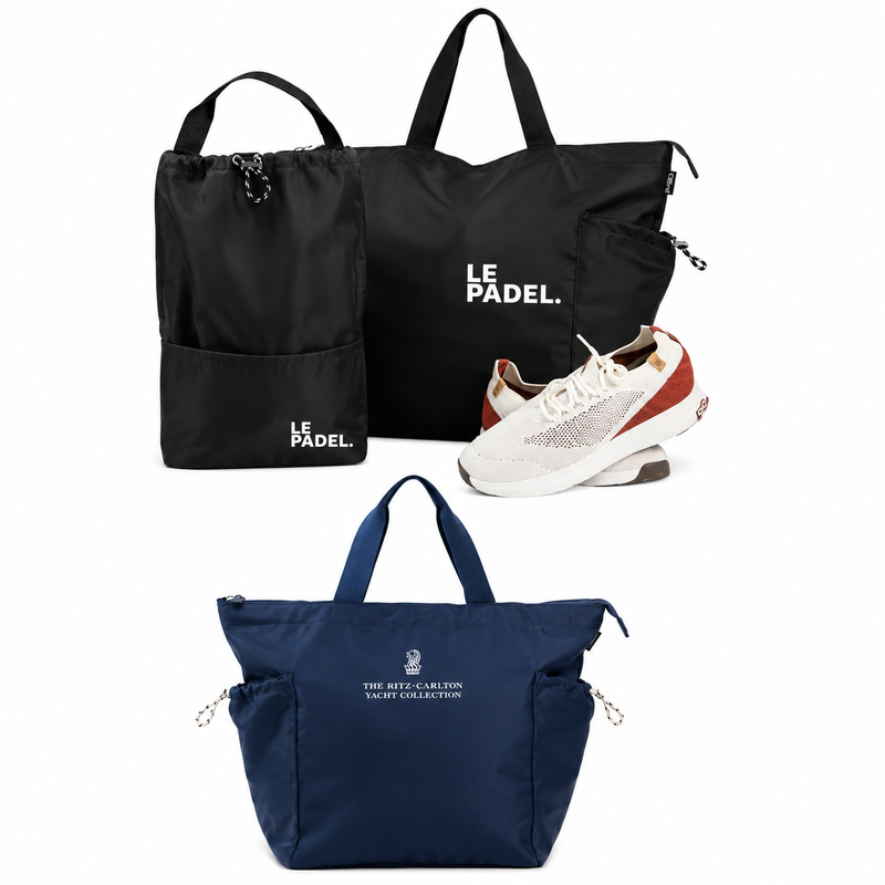 BYBBA tote and drawstring bags in black and navy, featuring LE PADEL and The Ritz-Carlton Yacht Collection branding, with a pair of white and brown athletic shoes.