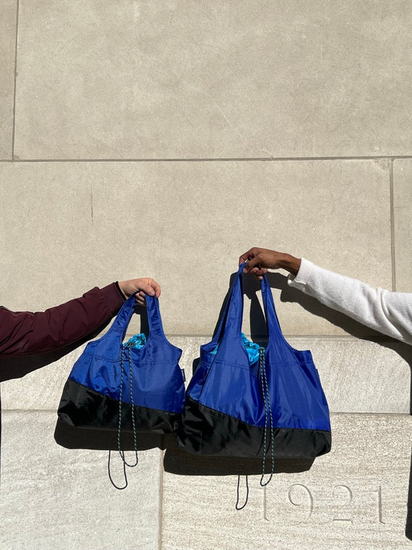 hands from two different people holding two sizes of deep blue bags
