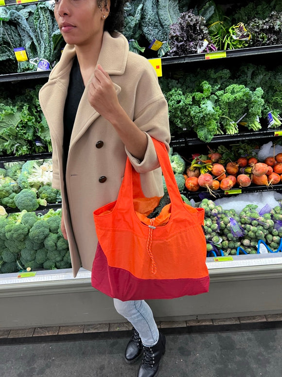 person in a produce section holding an orange bag